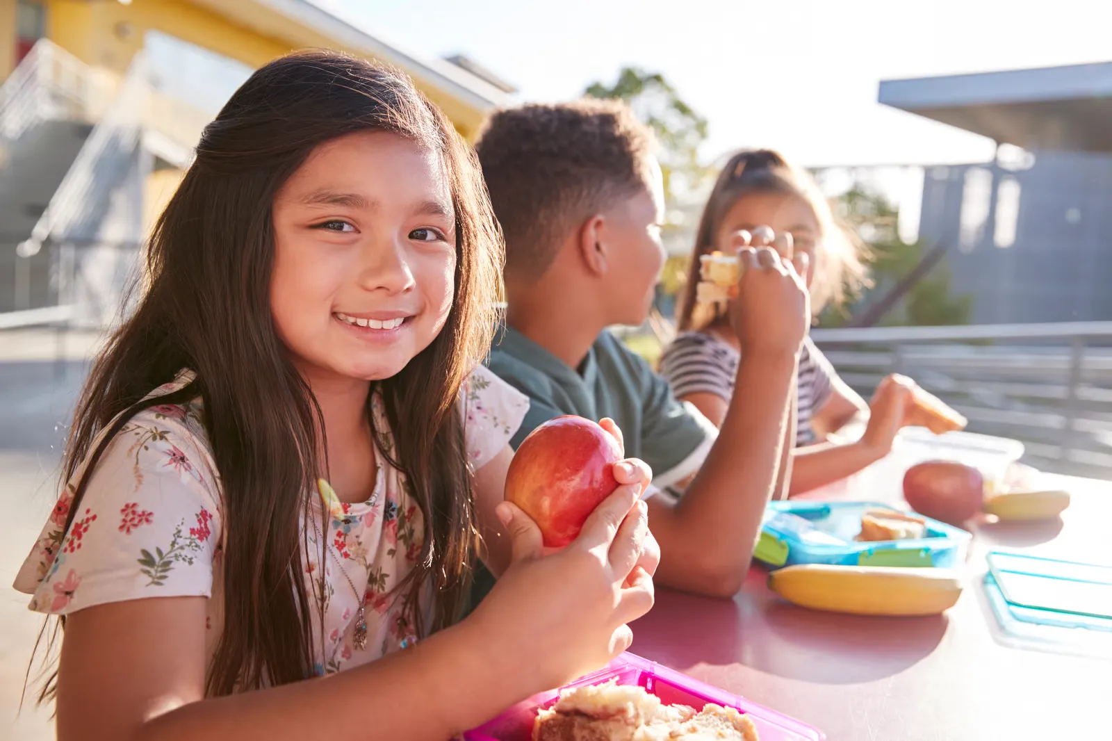 Niña sonriendo con una manzana durante la comida escolar